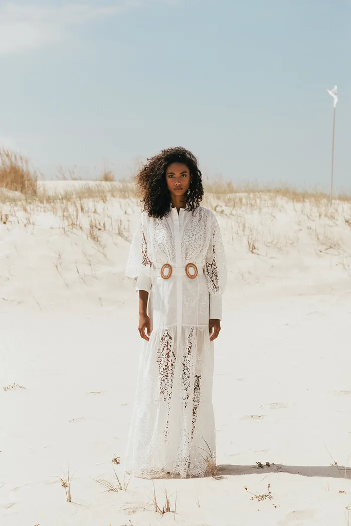 A woman in a white lace dress with a woven belt, standing on sand dunes