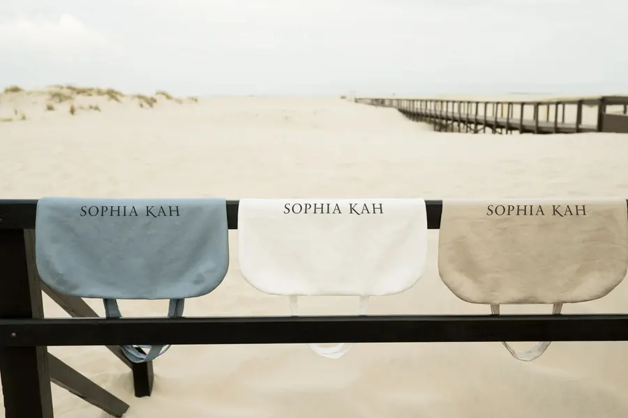 Three Sophia Kah linen bags in sky blue, white and sand, hanging on a beach fence