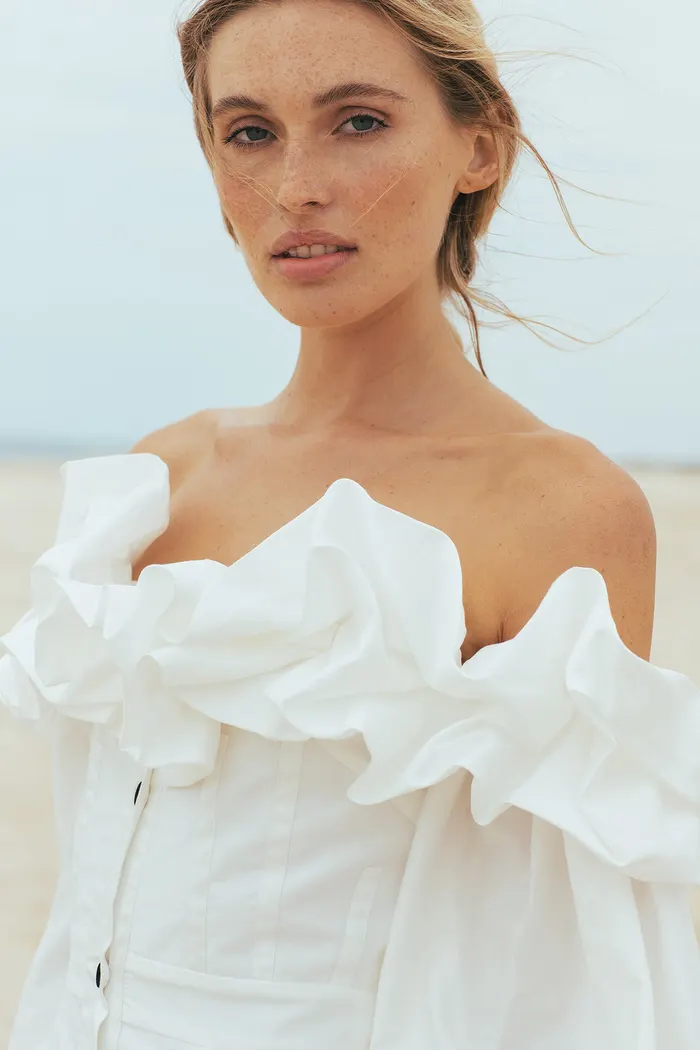 Portrait of a woman in a white ruffled off-shoulder top by the sea